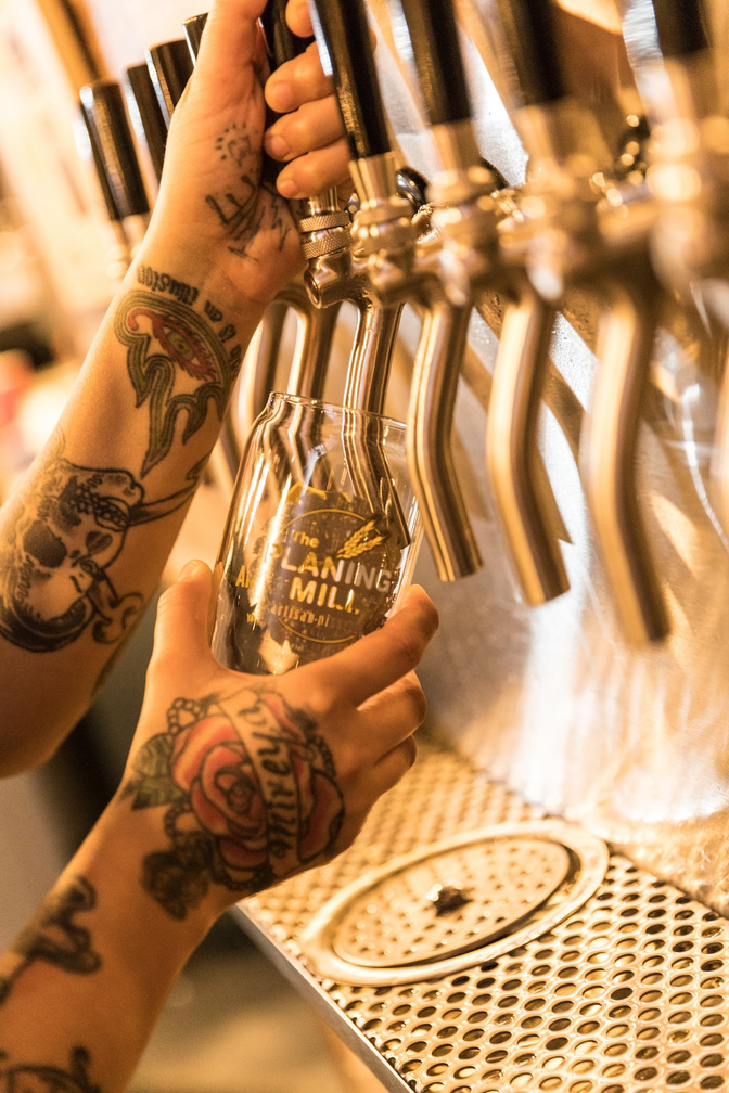 a person with tattoos pouring beer into a glass